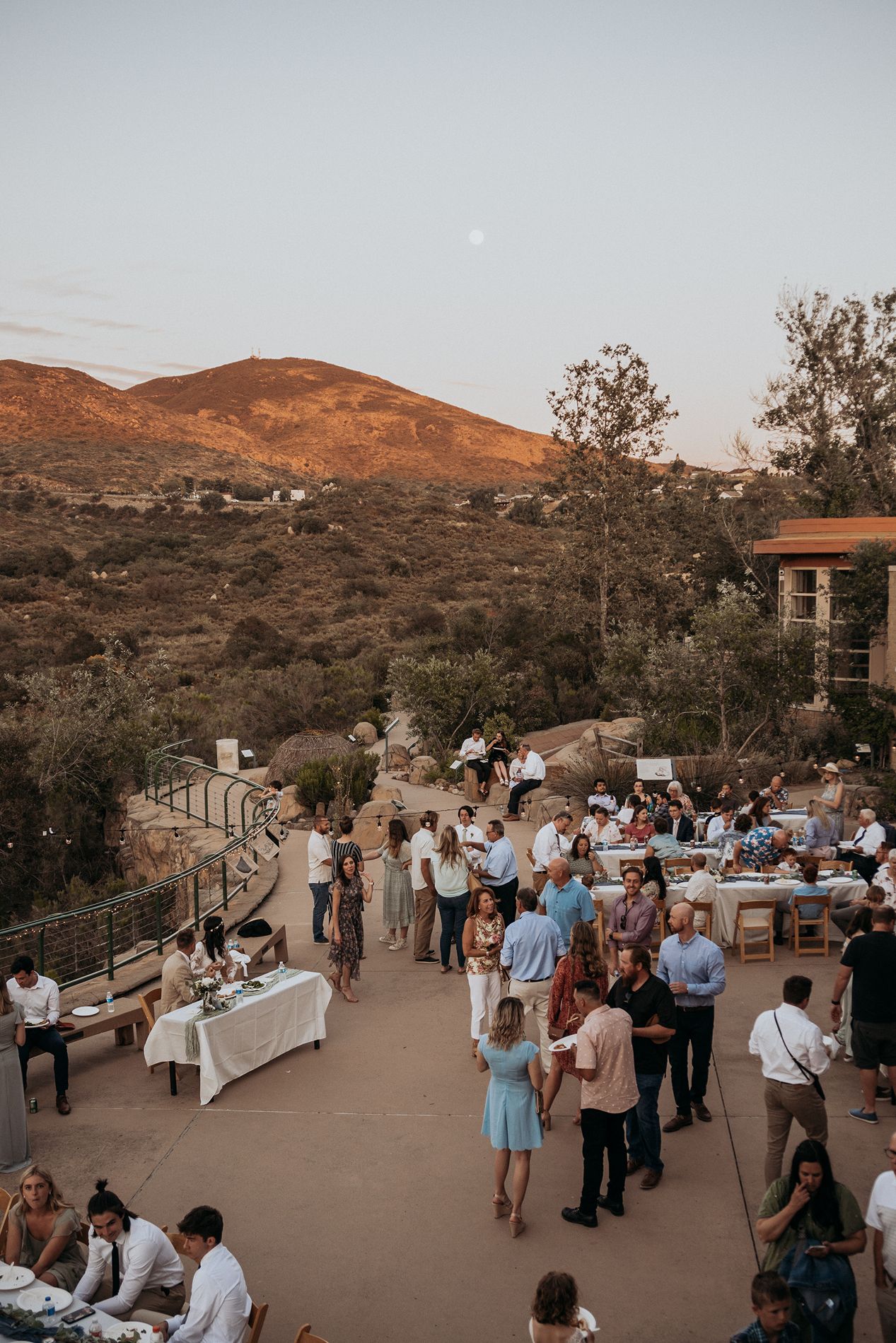 Outdoor evening gathering on a terrace with desert hills and a full moon backdrop at golden hour at Mission Trails Community Center.