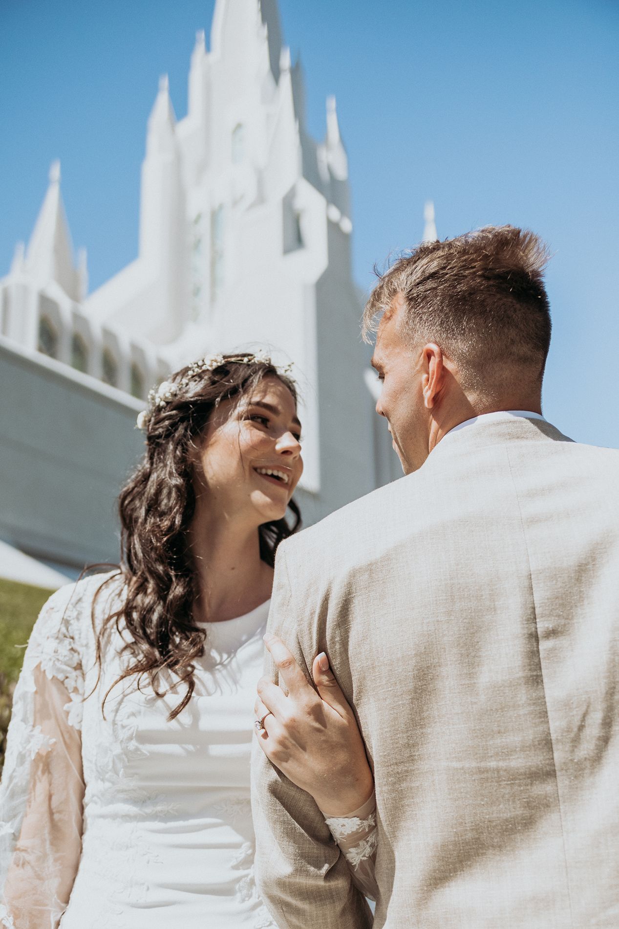 Bride and groom smiling at each other in front of a white LDS temple on a sunny wedding day in San Diego.