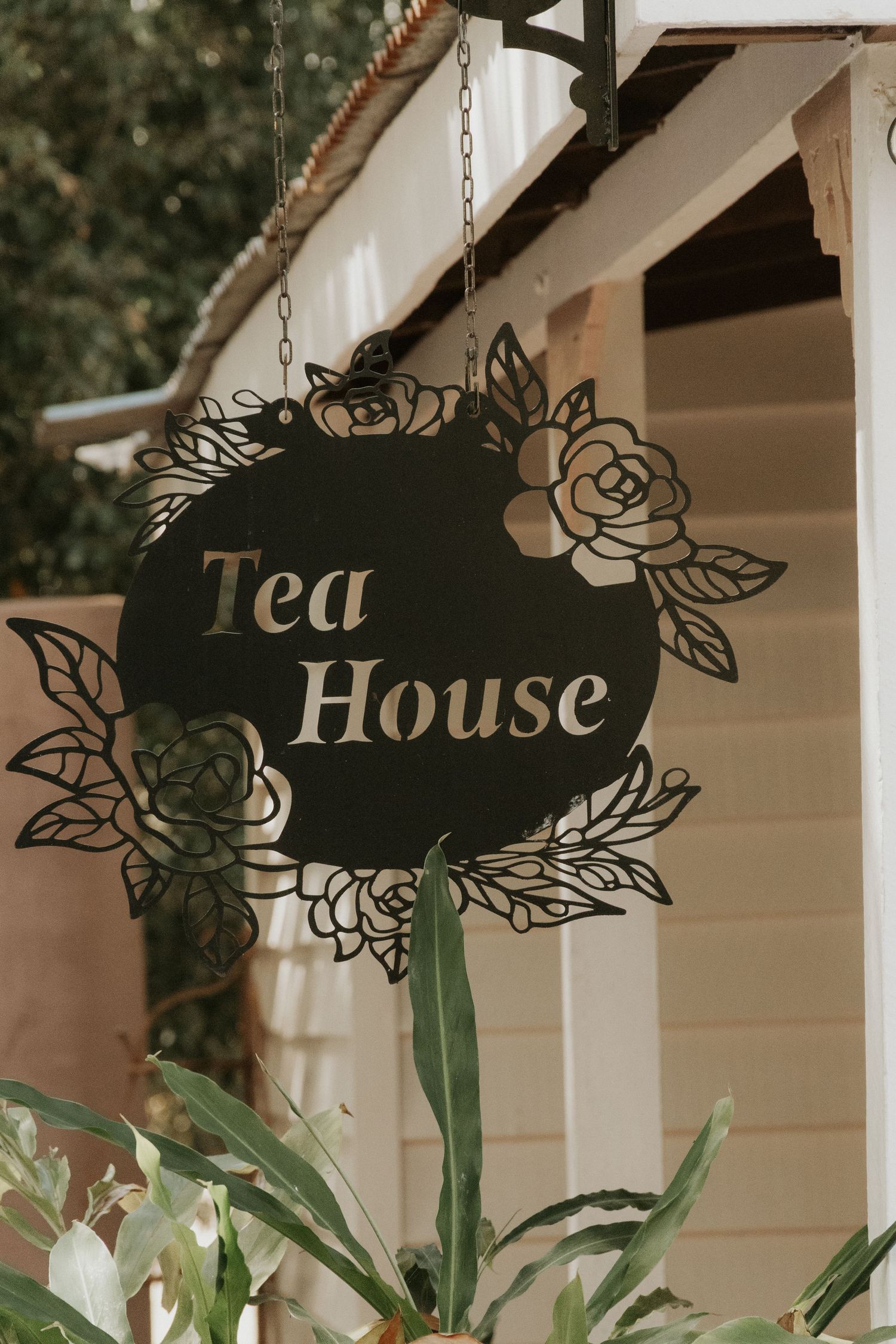 Decorative black metal Tea House sign with floral rose design hanging outside a building.