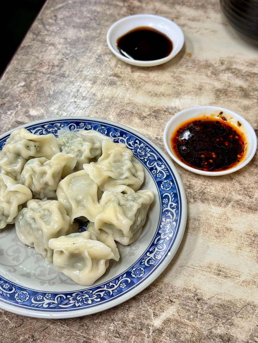 Plate of steamed Chinese dumplings on a blue and white plate served with soy sauce and chili oil dipping sauces.