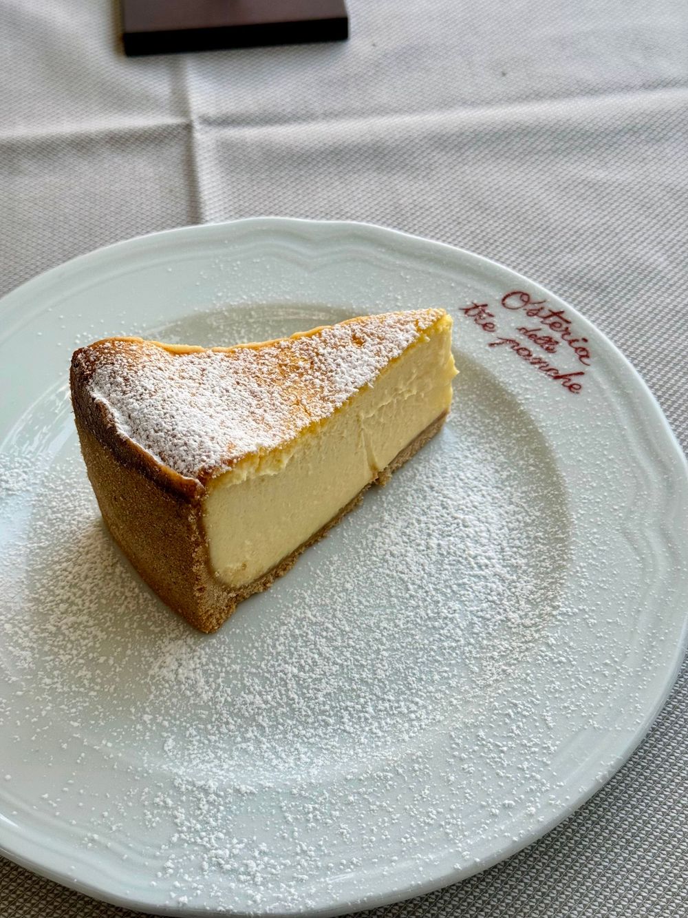 Slice of creamy cheesecake dusted with powdered sugar on a white plate at Osteria delle Tre Panche.