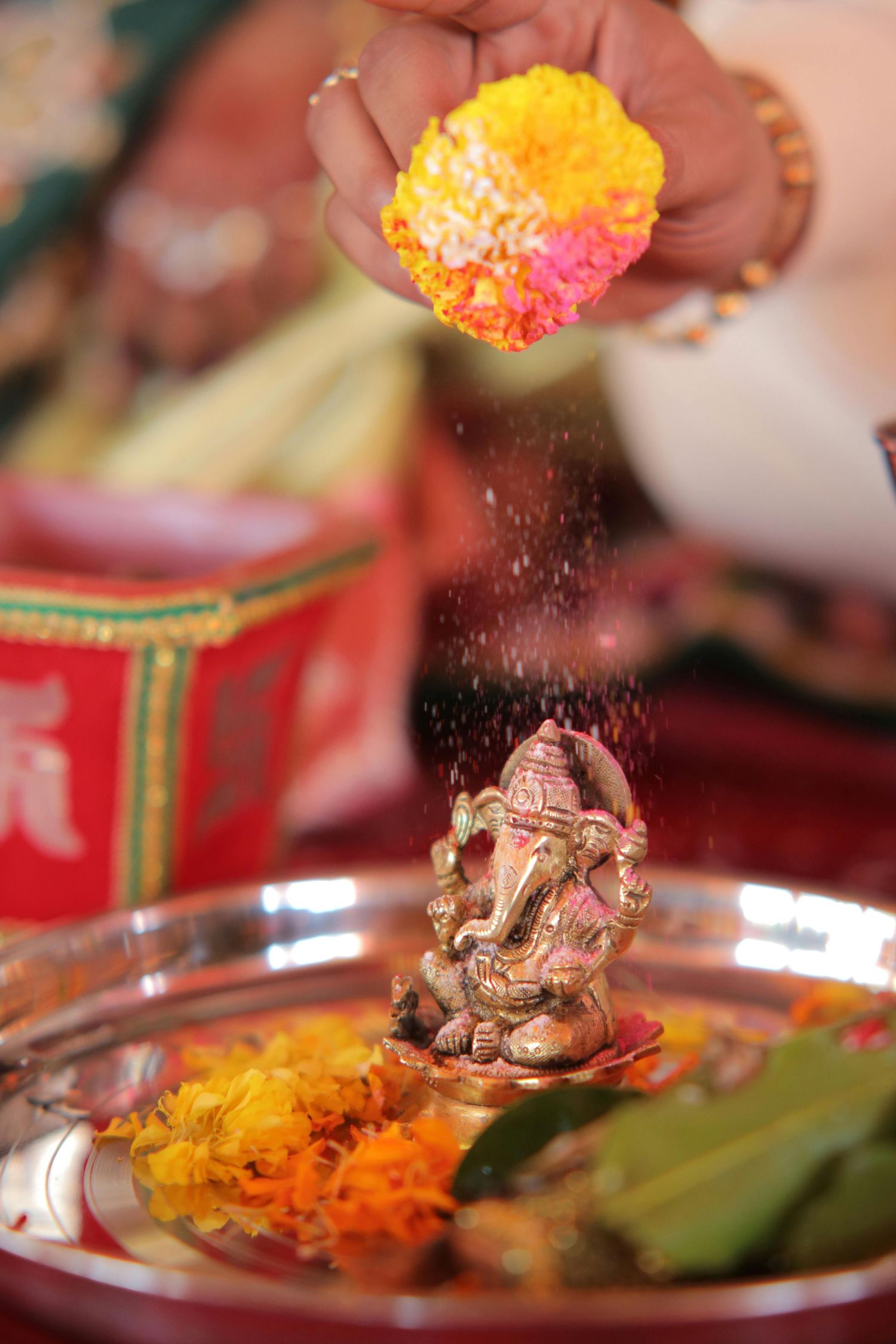 Hand offering flower petals over a gold Ganesha idol on a silver puja thali with marigolds during Hindu ritual.