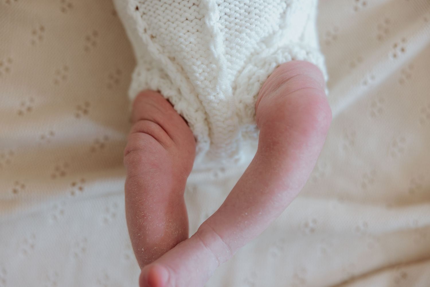 Close-up of newborn baby legs and feet resting on a soft white knitted blanket.