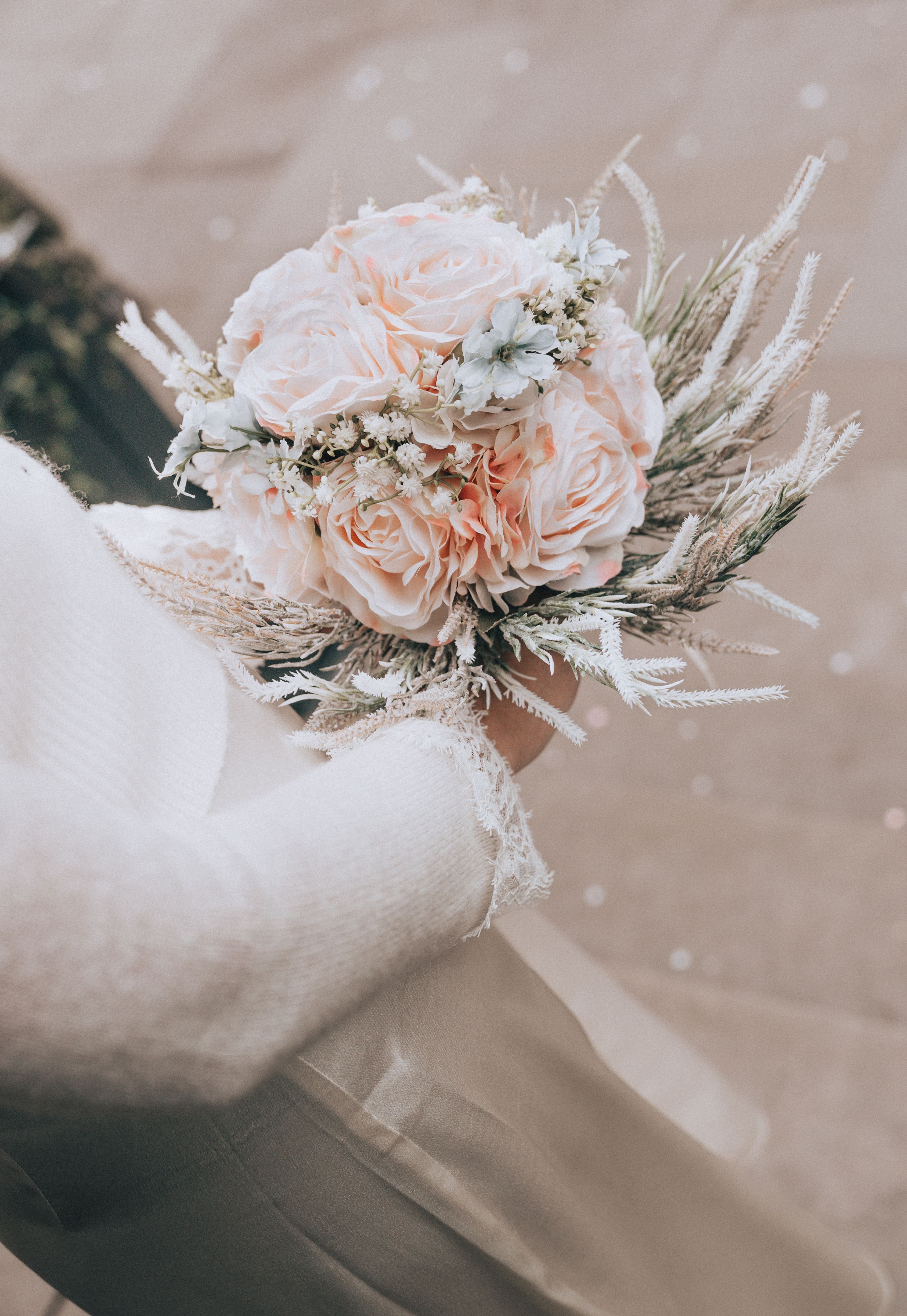 Bride holding a delicate bouquet of blush pink roses and dried flowers on wedding day.