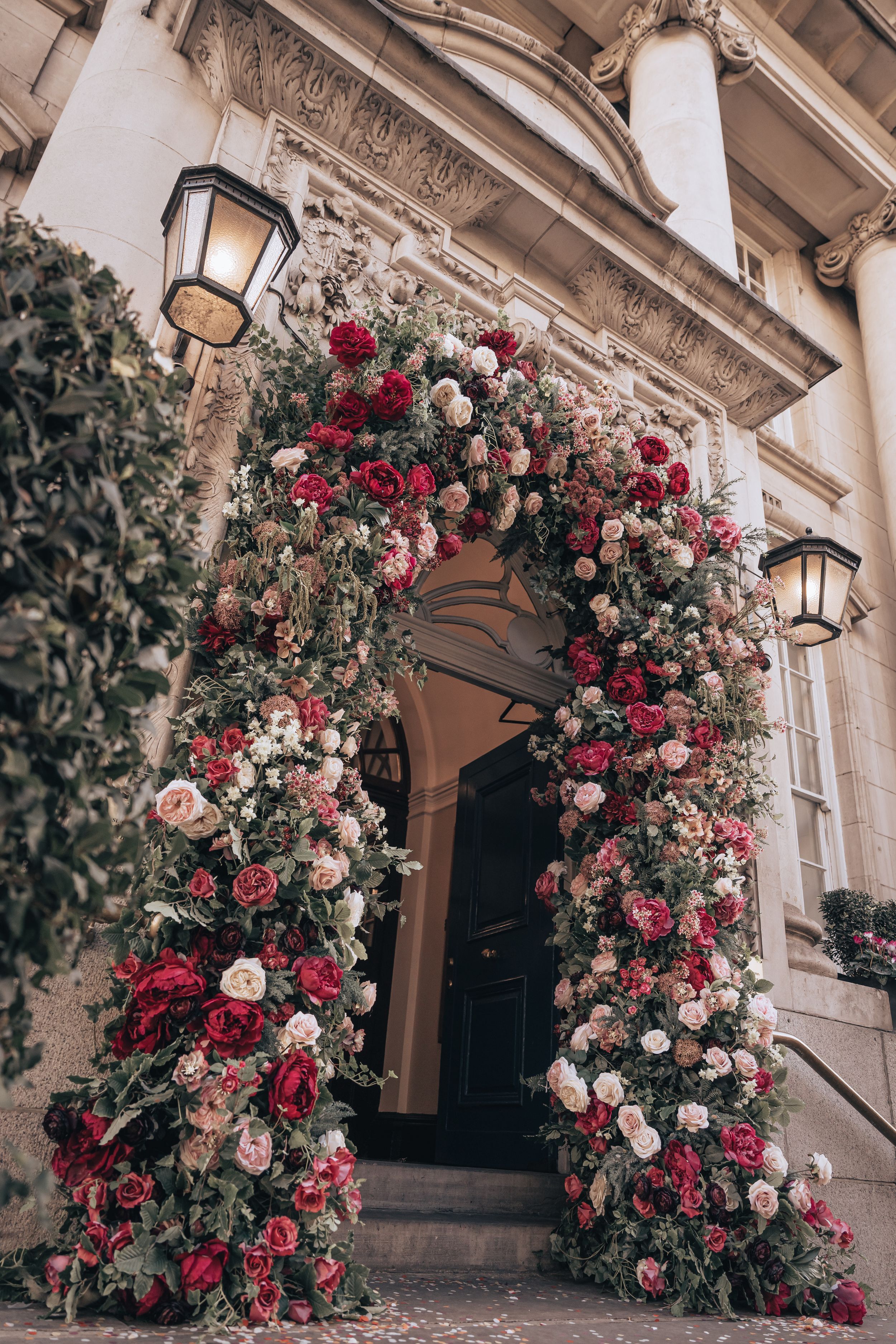 Elegant floral arch of Chelsea Old Town Hall with red and pink roses framing the grand building entrance.