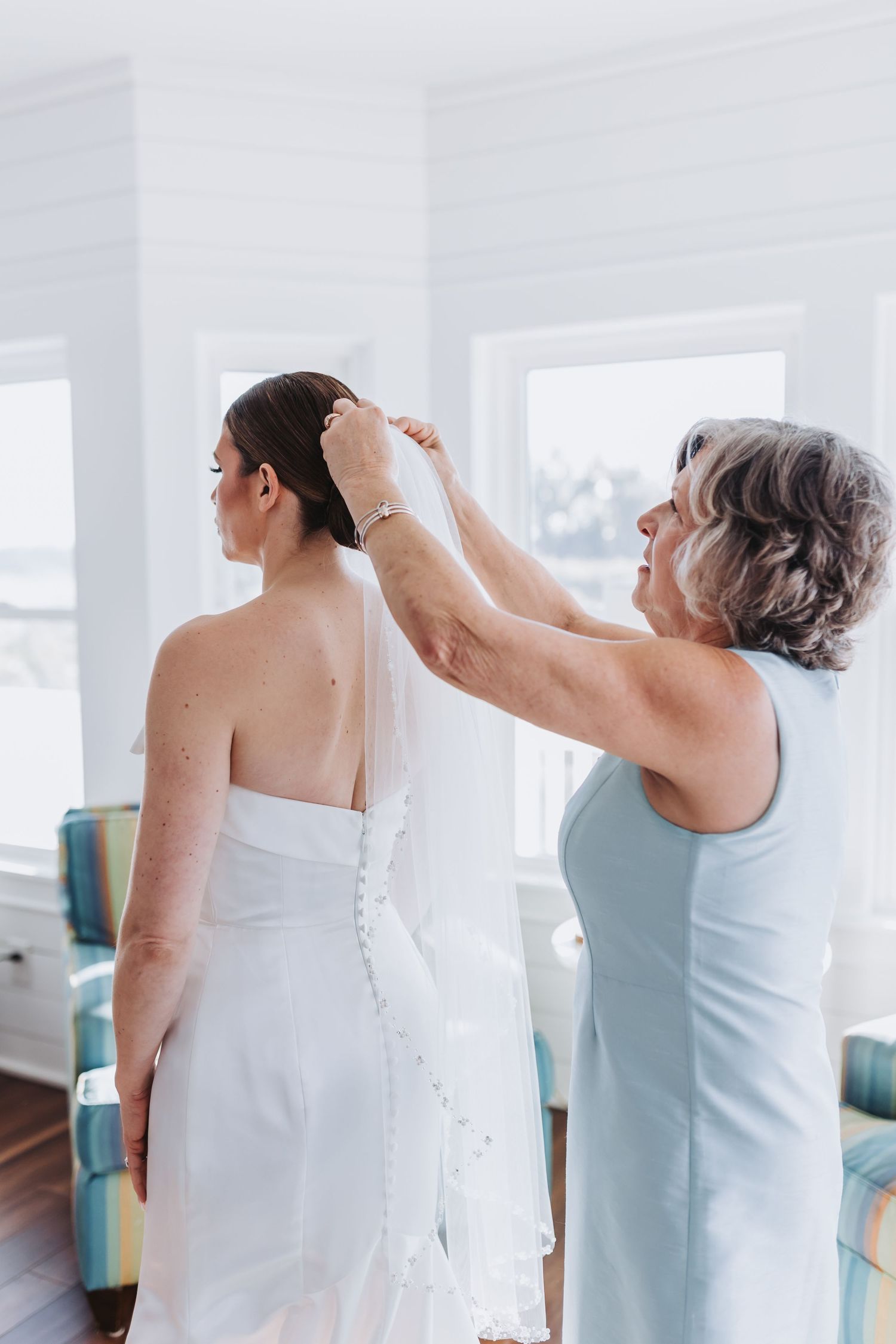 Mother helps bride secure veil in her updo before the wedding ceremony in a bright room.