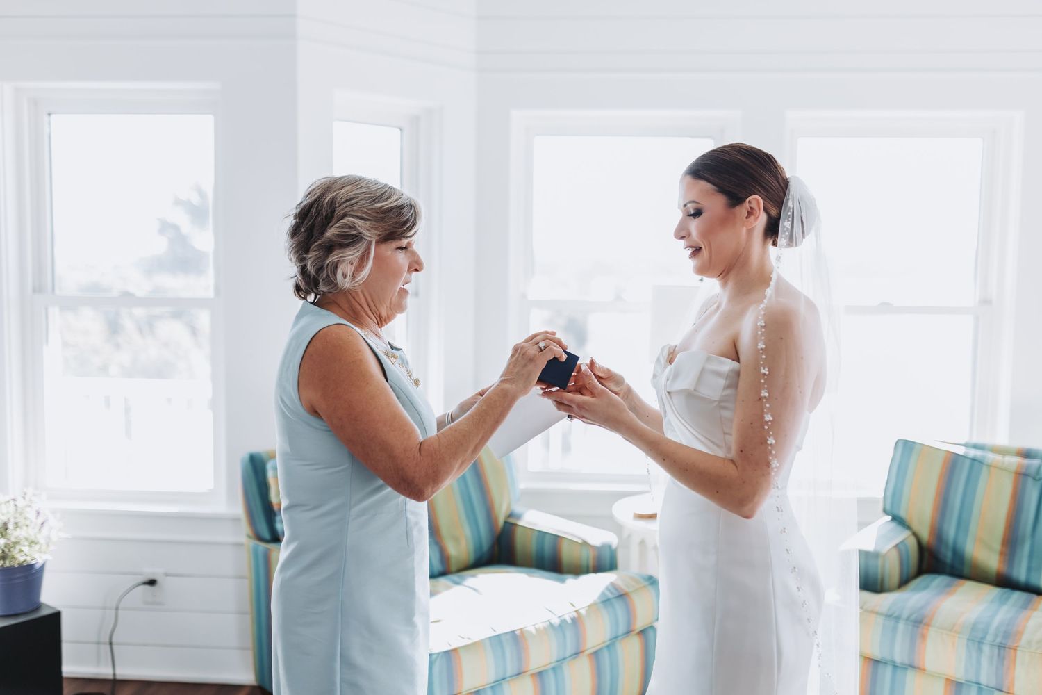 Mother of the bride presenting a jewelry gift box to her daughter in a strapless wedding gown.