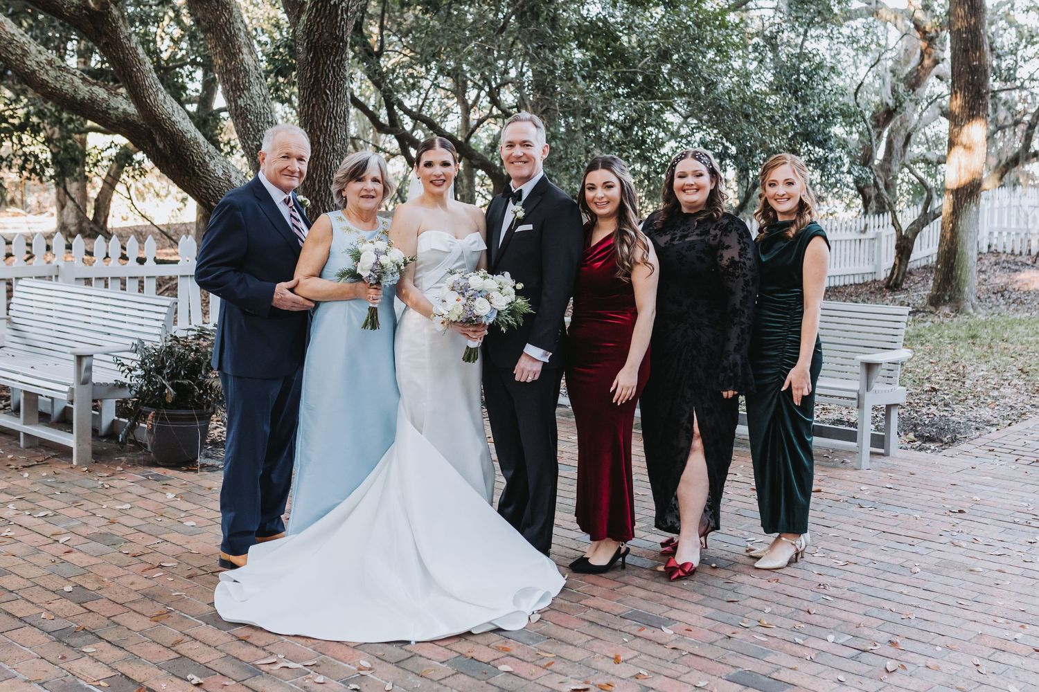 Wedding party group portrait outdoors on brick path with bride, groom, and family members.