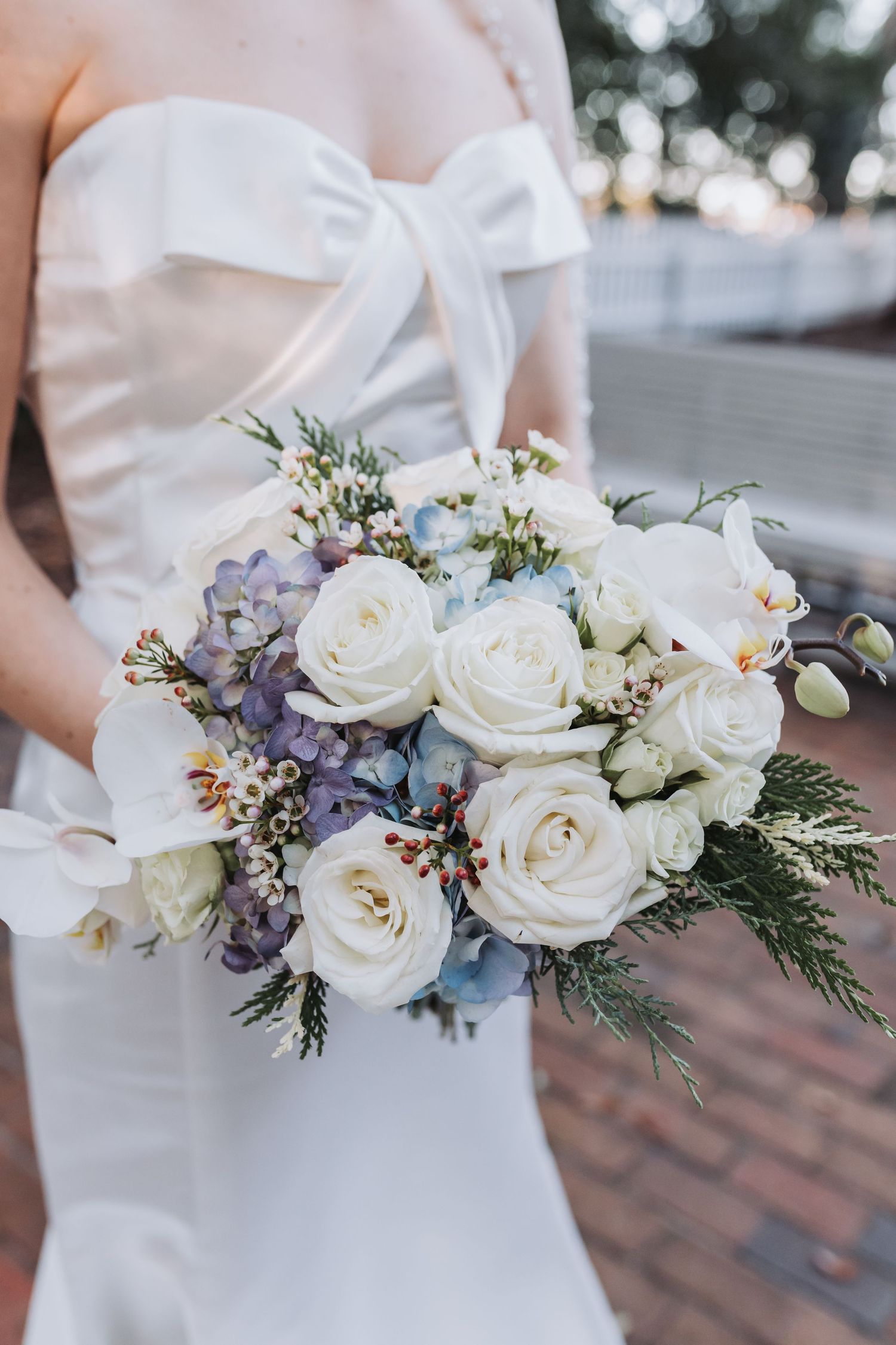 A bride holds a stunning bouquet of white roses, orchids, and blue hydrangeas in her wedding dress.