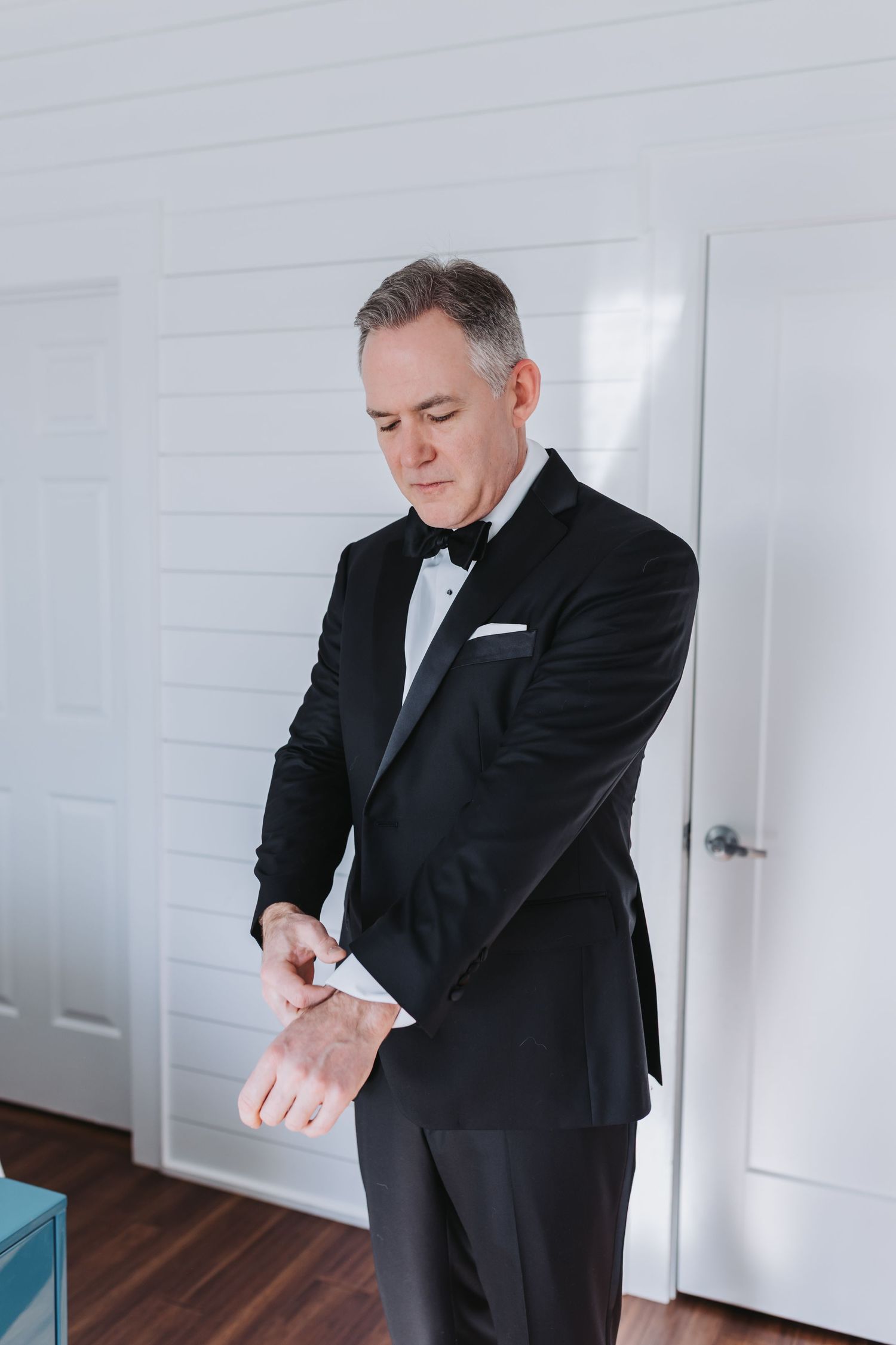 Dapper groom in black tuxedo and bow tie adjusting his cufflinks before the wedding ceremony.