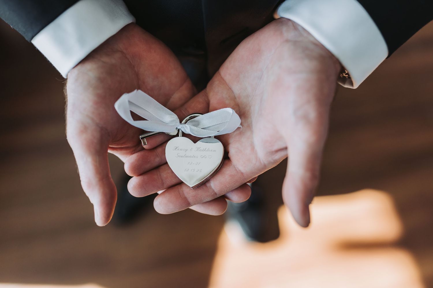 Groom holds a small wooden heart charm tied with ribbon in his hands before the wedding ceremony.
