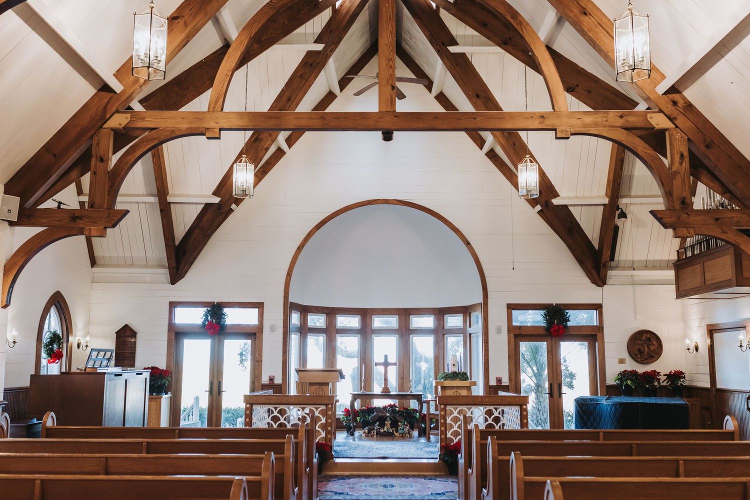 Elegant chapel interior with wooden pews, exposed timber trusses, and arched windows decorated for a winter wedding.