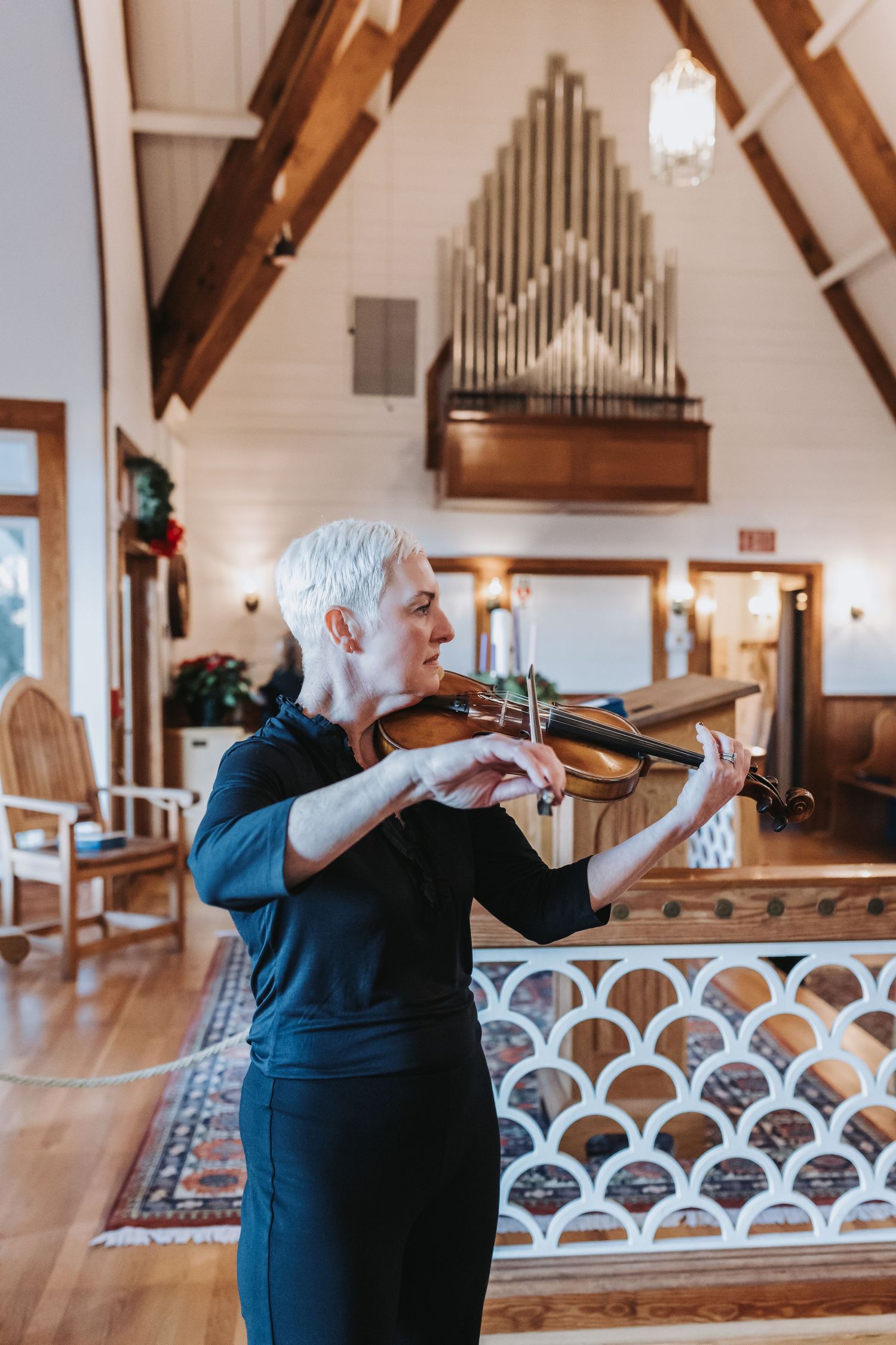 Elegant violinist in black dress performs in rustic chapel with wooden beams and pipe organ backdrop.