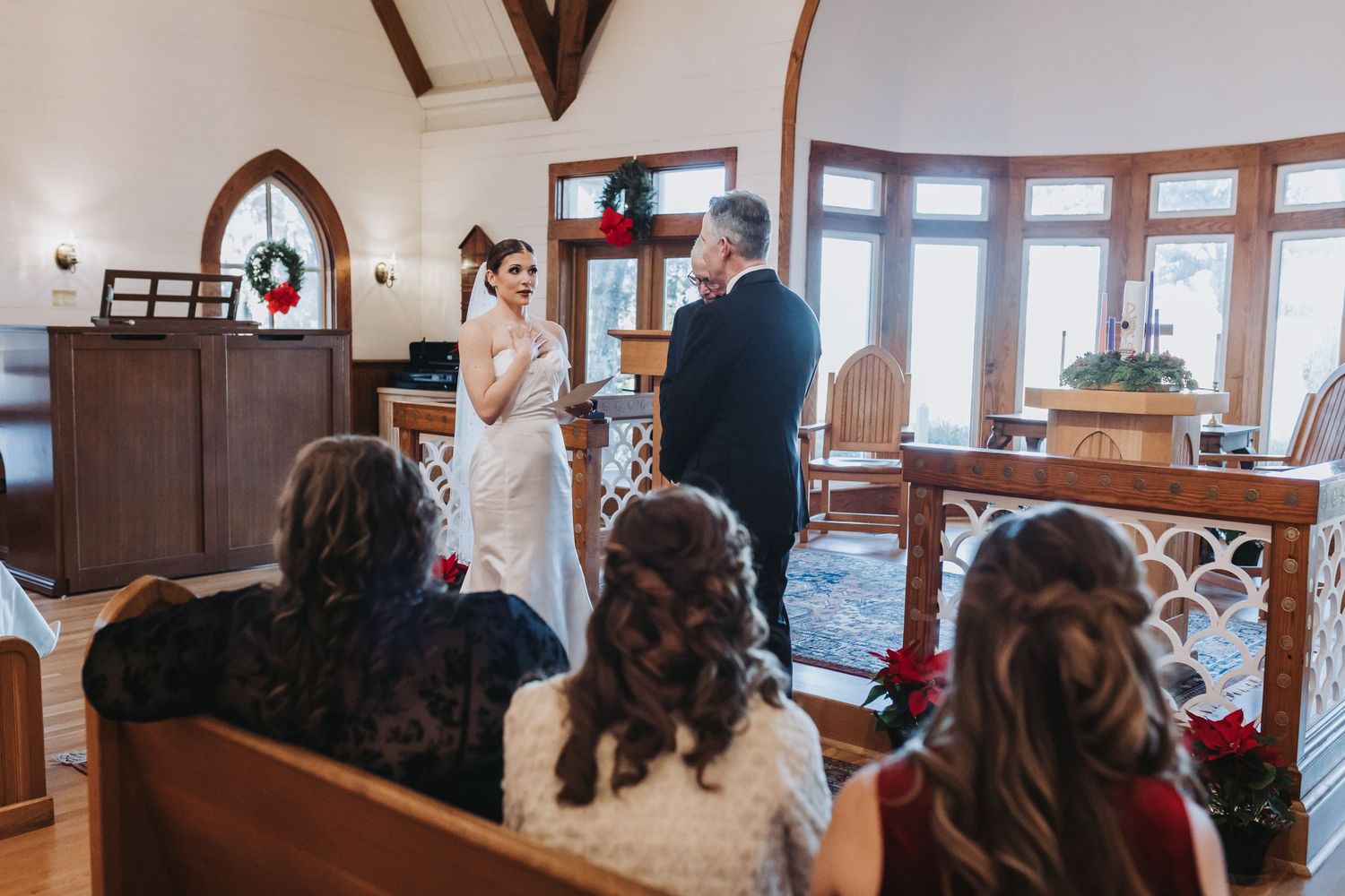 A bride and groom exchange vows at a Christmas-decorated intimate chapel wedding ceremony.