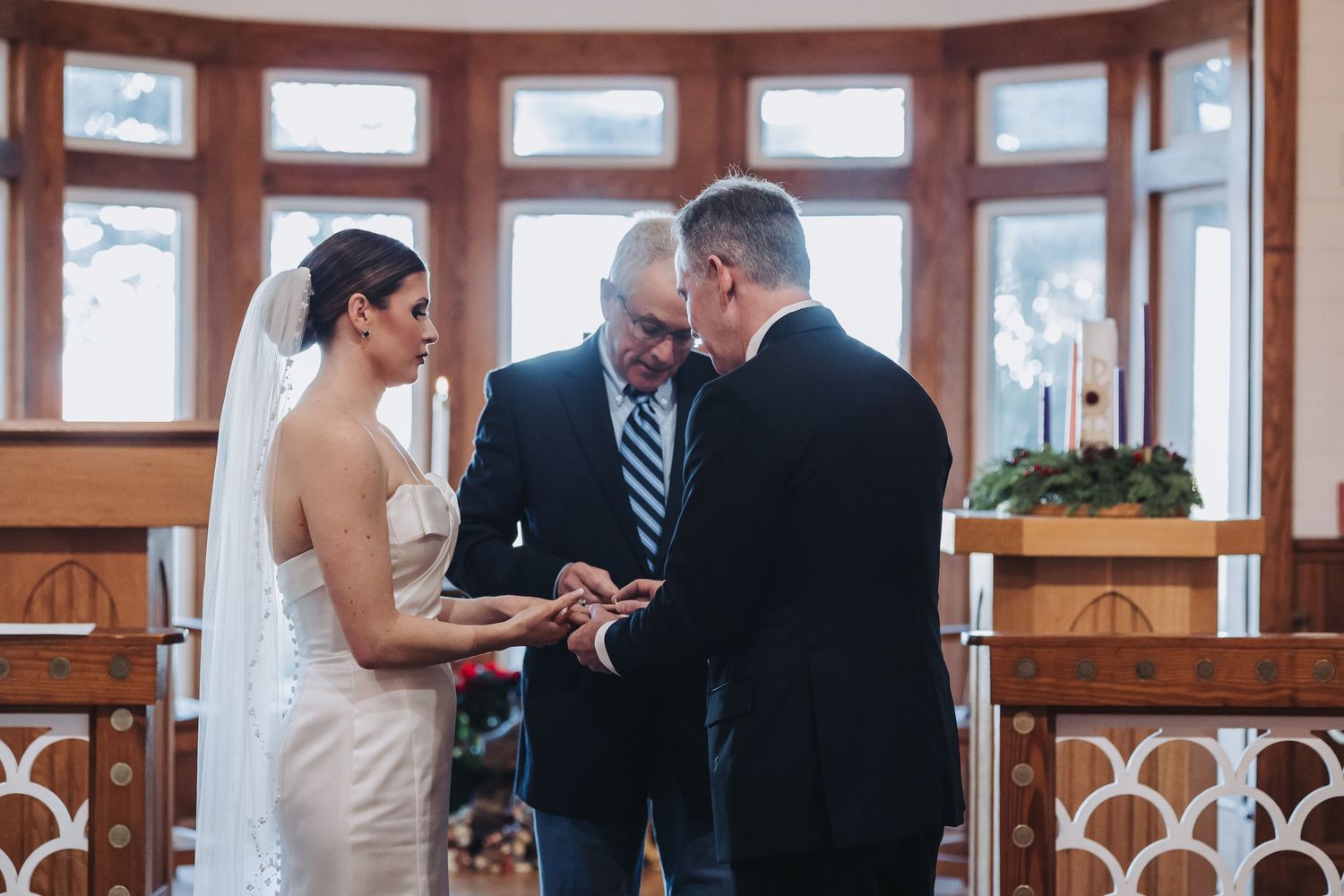 Bride and groom exchange rings at chapel altar during intimate winter wedding ceremony with officiant.