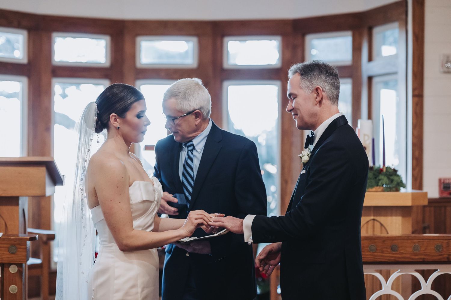 Bride and groom exchange rings at the altar with officiant during intimate chapel wedding ceremony.