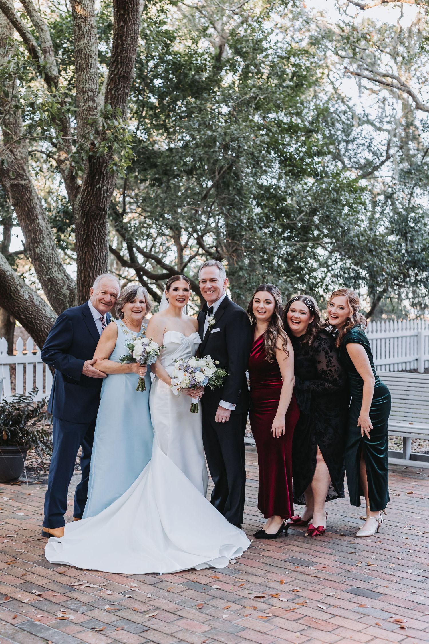 Bride and groom celebrating with family outdoors under oak trees on a brick patio after their wedding.