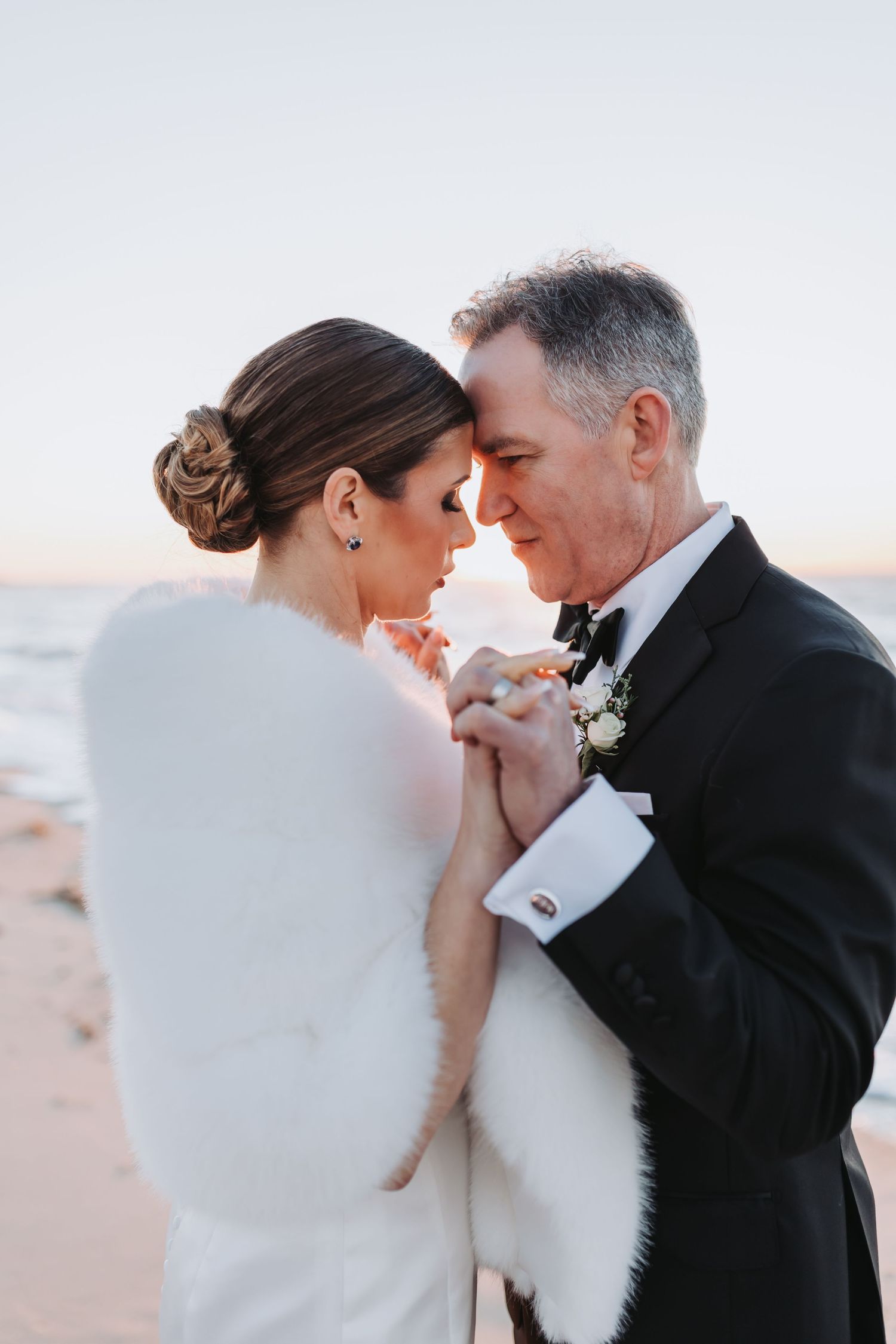 Bride and groom sharing an intimate moment on the beach at sunset, holding hands and touching foreheads.