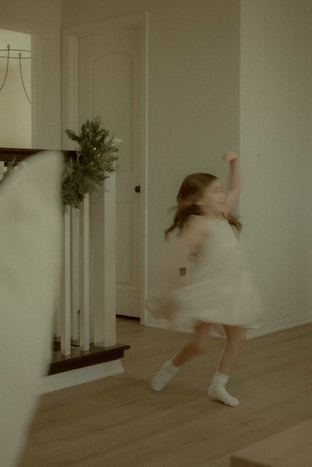Young girl in a white dress twirling and dancing in a bright home hallway.