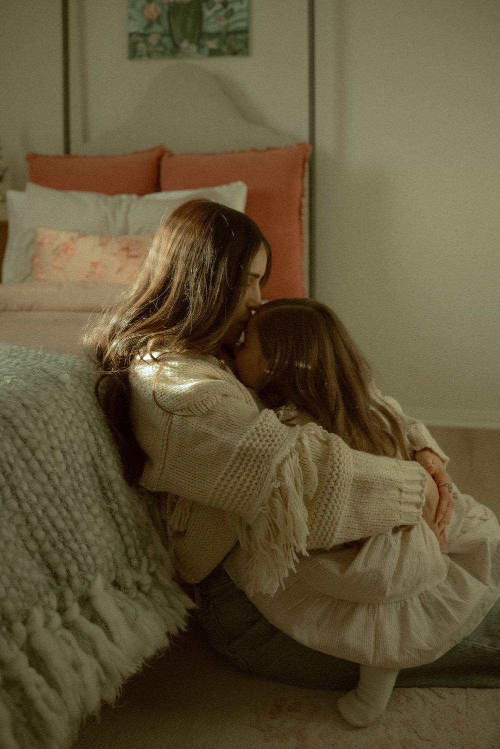 Mother and daughter sharing a tender forehead-to-forehead moment while sitting on the floor beside a bed.