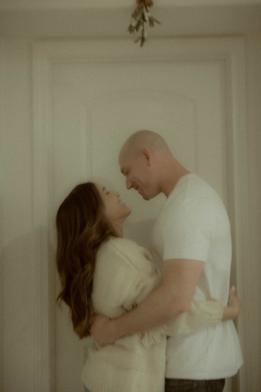 Couple sharing an intimate moment, leaning close together under mistletoe in front of a white paneled door.