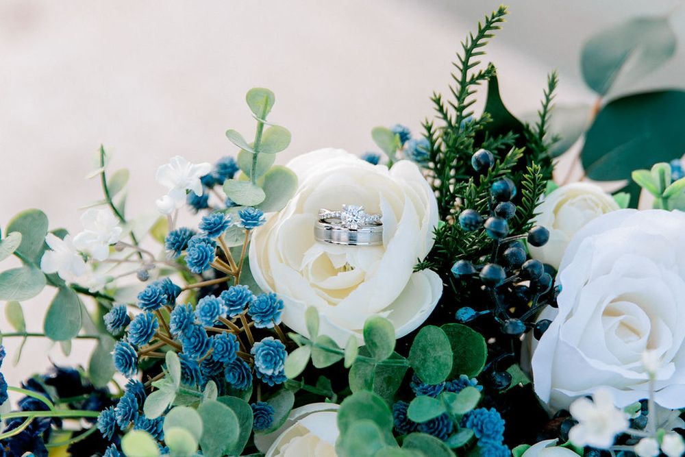 Wedding rings nestled in white roses with blue berries and eucalyptus in a bridal bouquet.