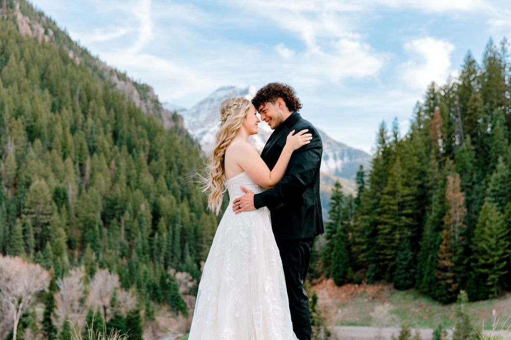 Bride and groom embrace romantically with mountain forest backdrop on their wedding day.