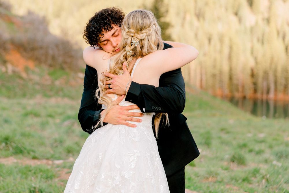 A bride and groom share a tender embrace outdoors, with the bride in a lace gown and groom in a black suit.