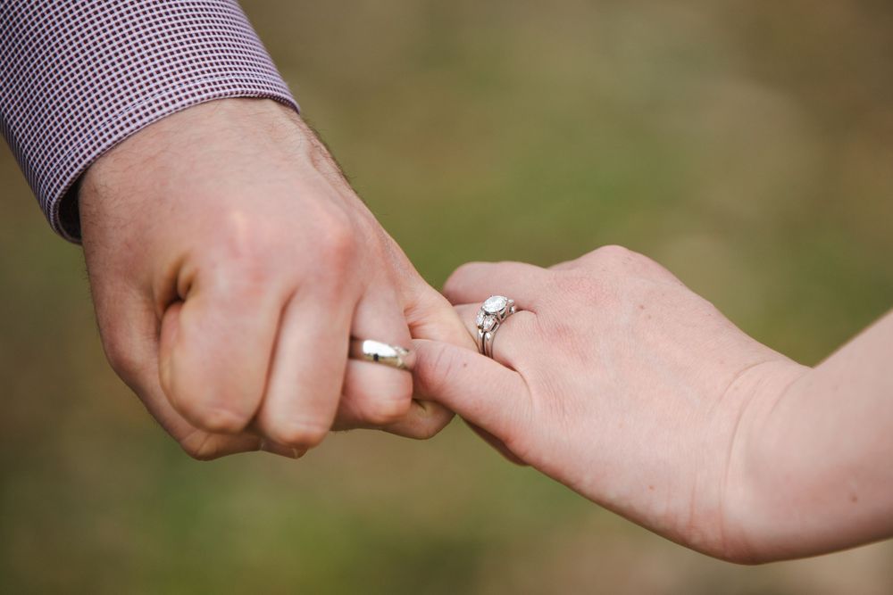 Couple holding pinkies showing matching silver wedding rings, symbolizing love and commitment.
