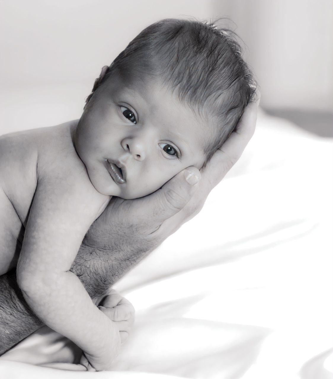A black and white close-up portrait of a newborn baby lying on a white blanket.