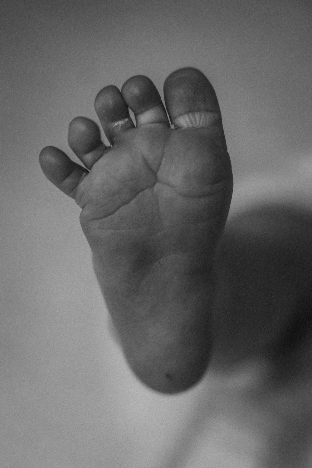 Close-up black and white photo of a newborn baby's tiny foot sole showing delicate skin creases and small toes.