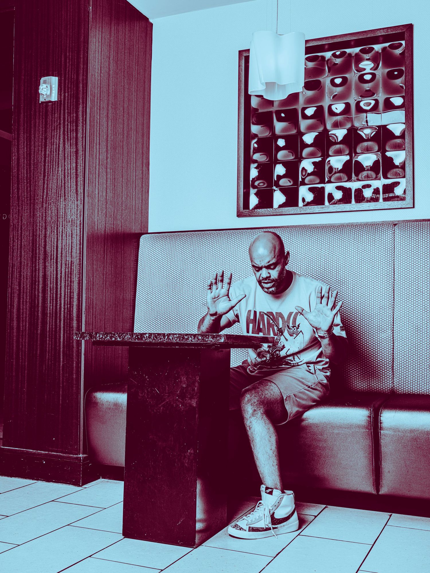 Man in Hardcore t-shirt sitting at a diner booth table with hands raised, blue-tinted photo.