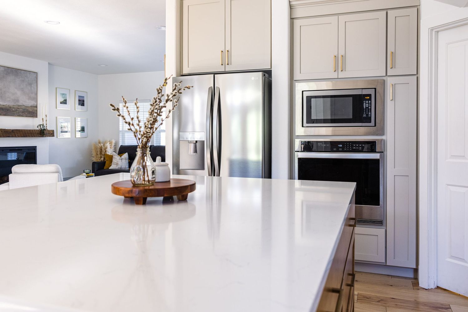 Modern white kitchen island with quartz countertop, gray cabinets, and stainless steel appliances in background.