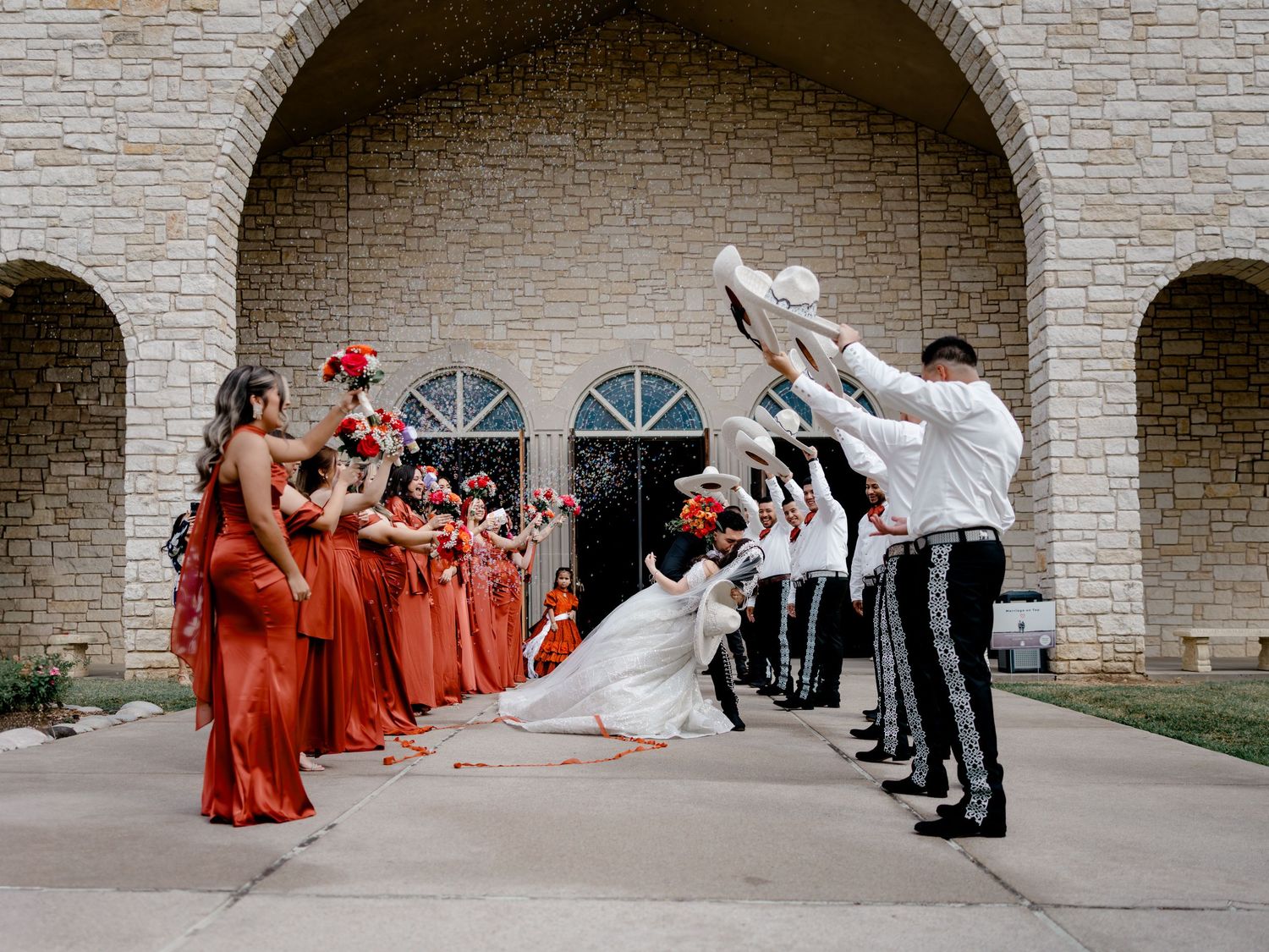 Traditional Mexican wedding exit in Carrollton, Texas. Groom in a Charro suit dips the bride as guests toss sombreros and flower petals.