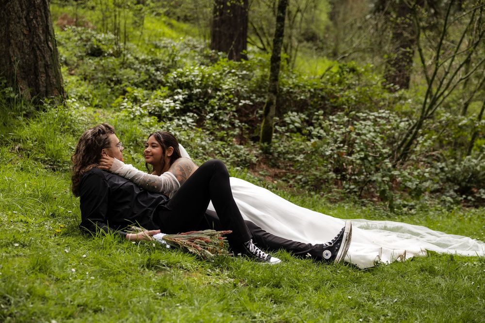 Bride and groom relaxing together on a grassy forest hillside surrounded by lush green foliage.
