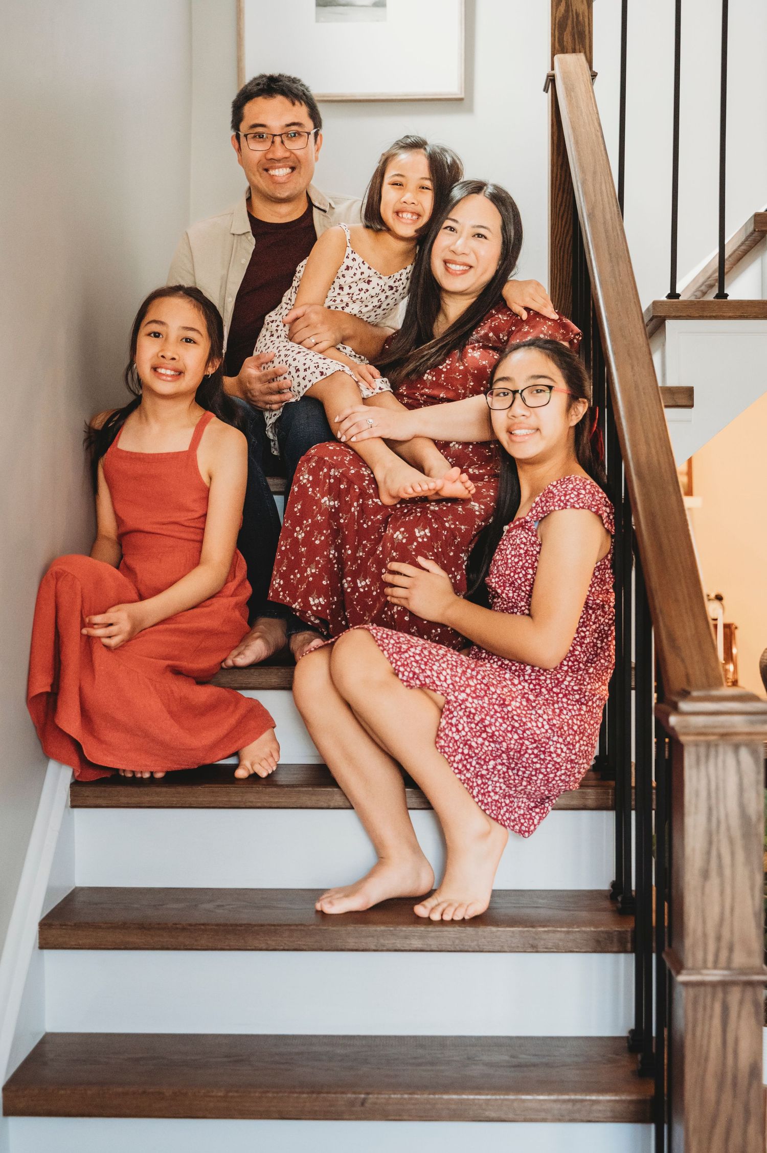 Family of five sits closely on stairs in their home smiling at the camera.