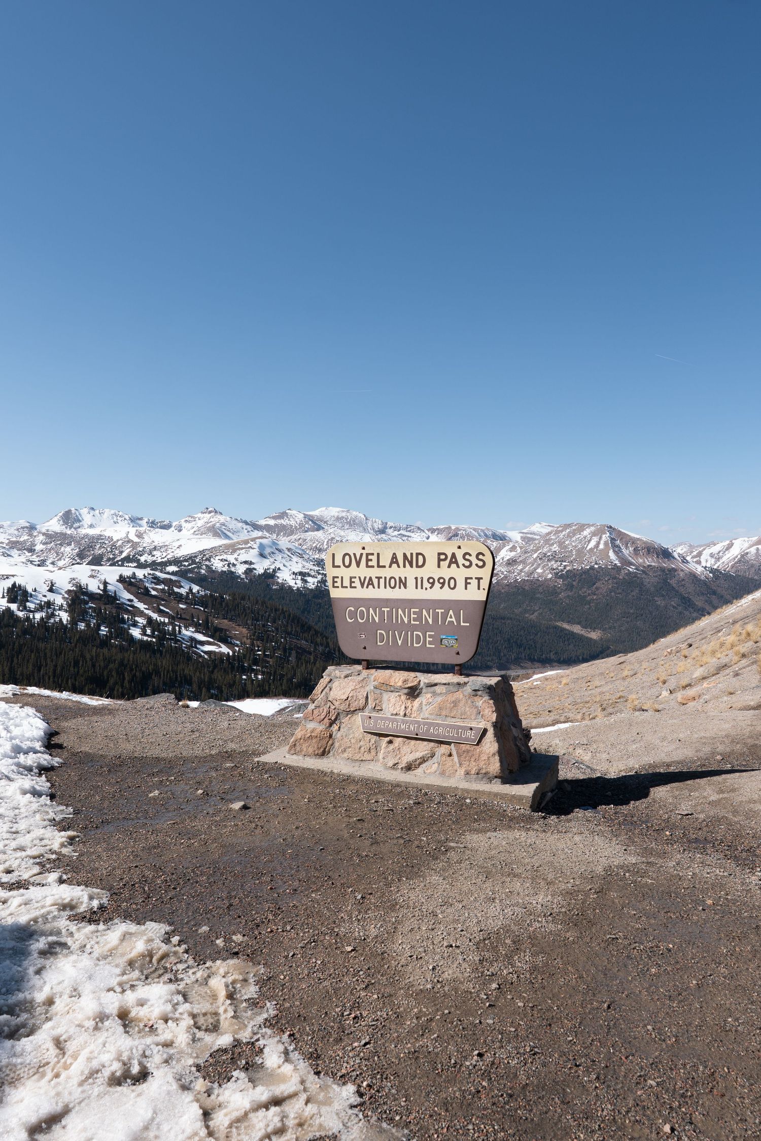 Loveland Pass elevation 11,990 ft Continental Divide sign with snow-capped Rocky Mountains and clear blue sky.