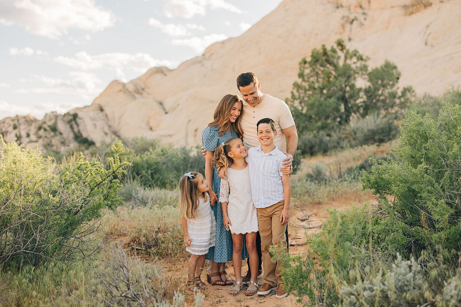 Family of five sharing a tender moment on a sandy trail surrounded by desert shrubs and rocks.