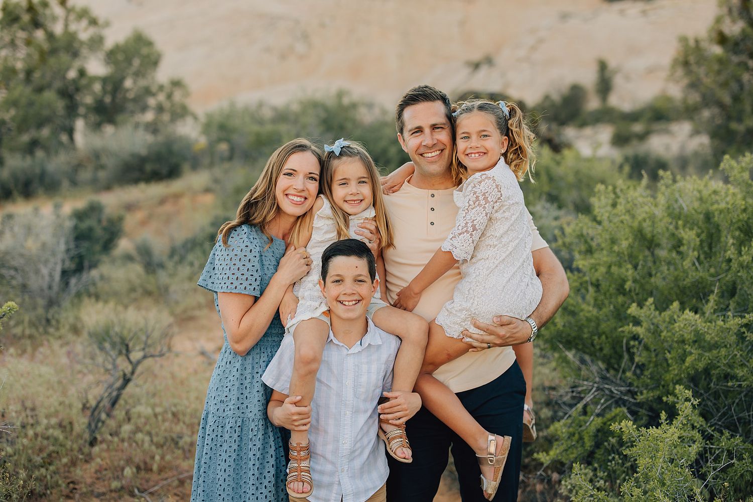 Happy family of five smiling outdoors in a desert landscape during a professional photo session.