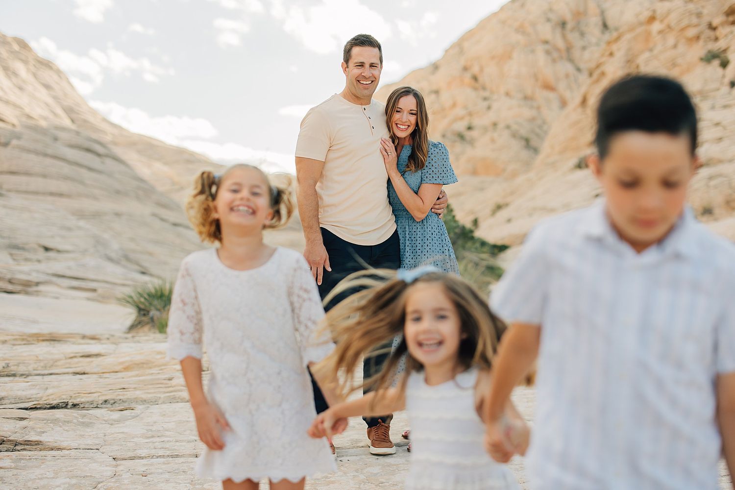 A happy family of five poses in a desert canyon, parents smiling as three children run toward the camera.
