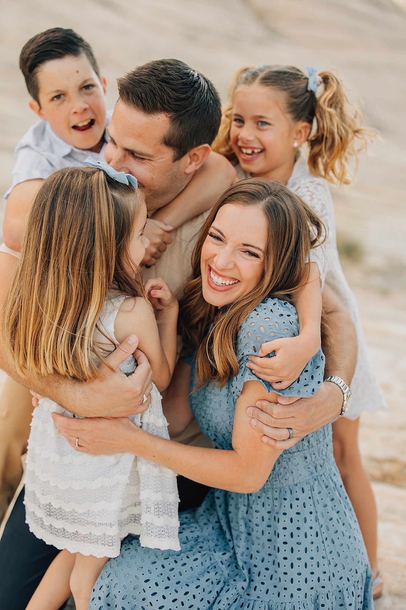 Joyful family of five hugging and laughing together outdoors in sandy desert setting.