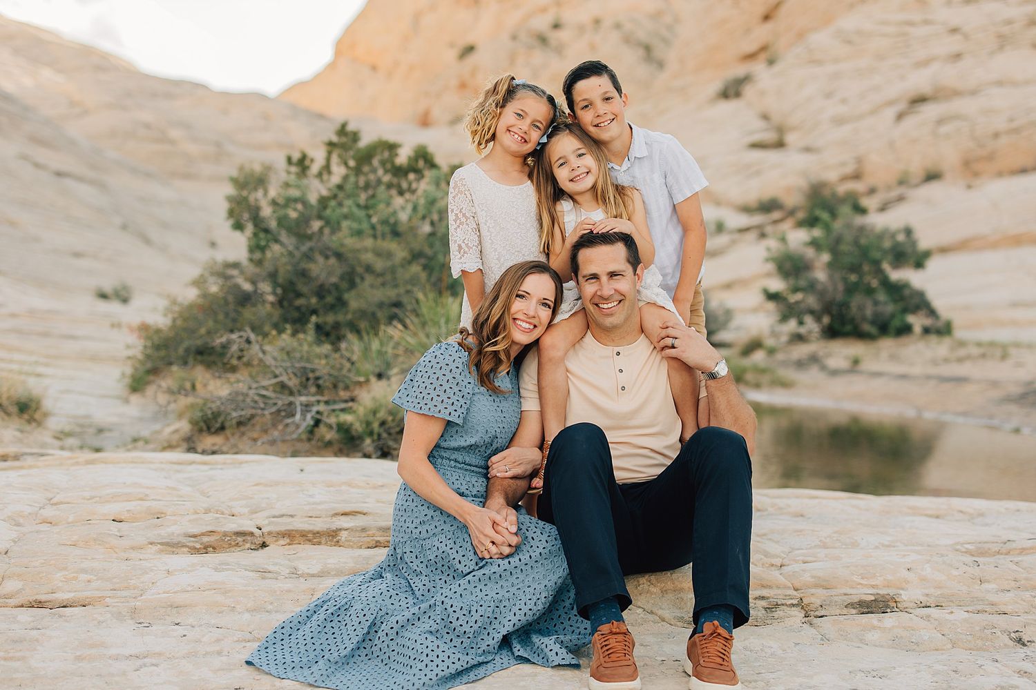 Family of four smiling together on rocky desert landscape during golden hour outdoor photo session.
