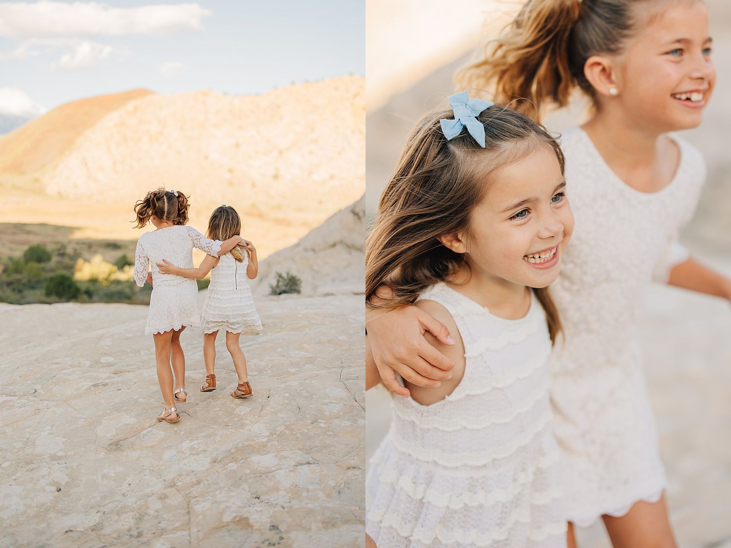Two young girls in white lace dresses embrace outdoors in a sandy desert landscape during golden hour.