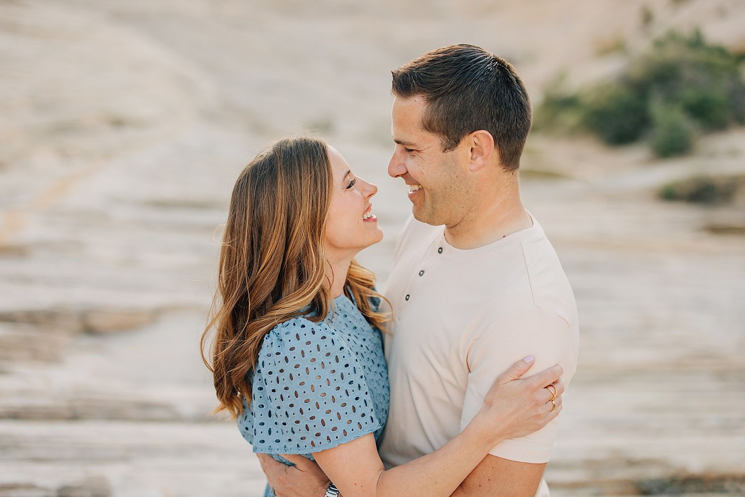 Happy couple embracing and smiling at each other in a romantic outdoor desert photo session.