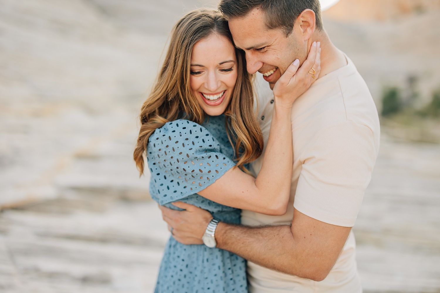 Joyful couple embracing and laughing together outdoors in a warm sunlit rocky landscape.