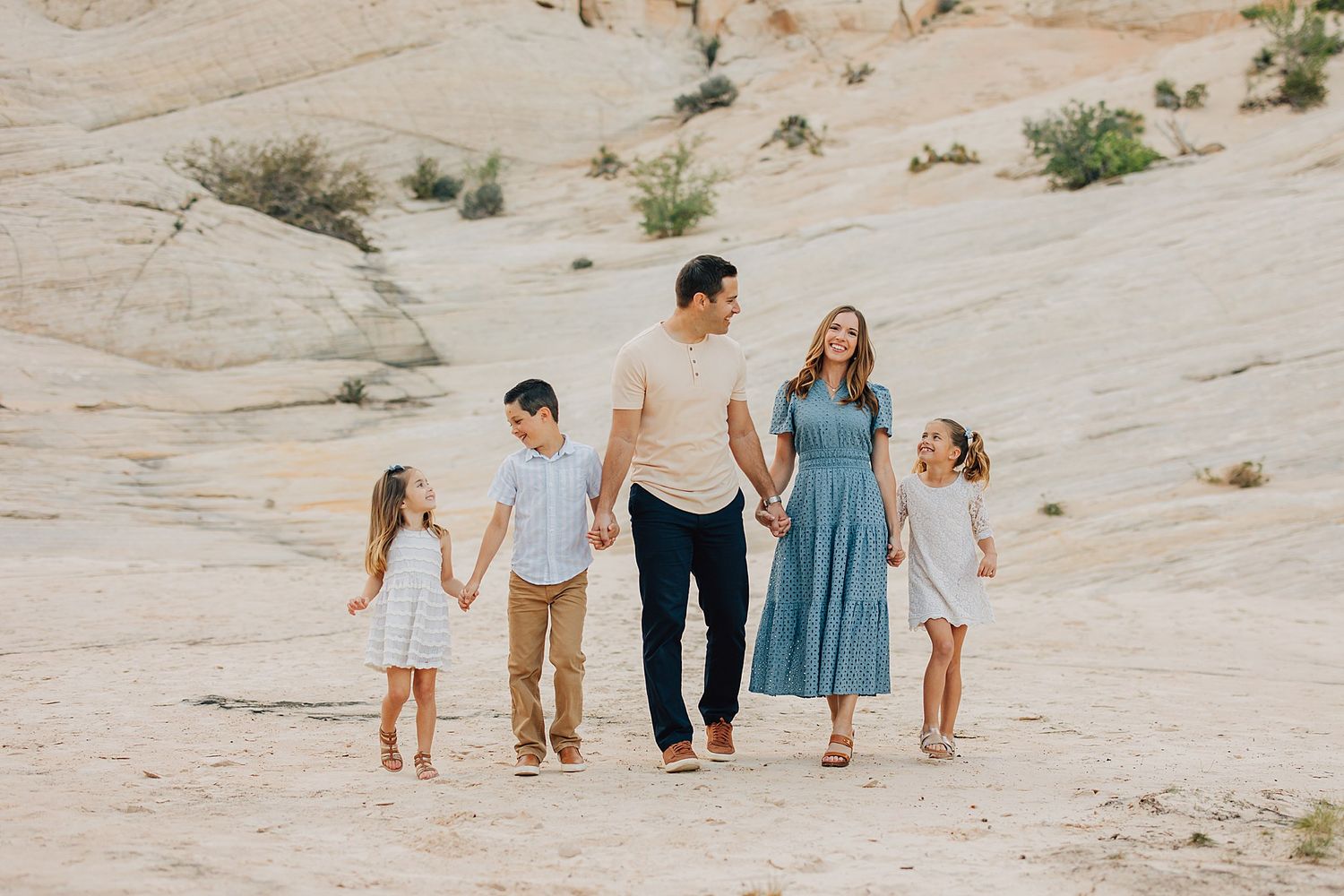 Happy family of five holding hands and walking together across a scenic desert landscape.
