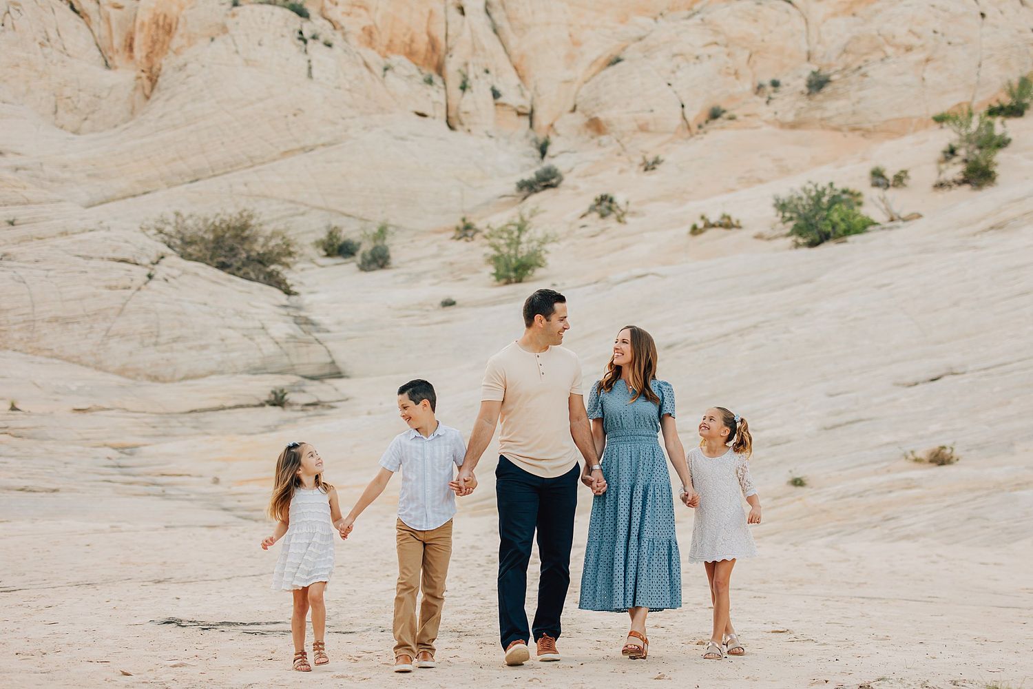 Family of five holding hands walking in a sandy desert landscape with white rock formations.