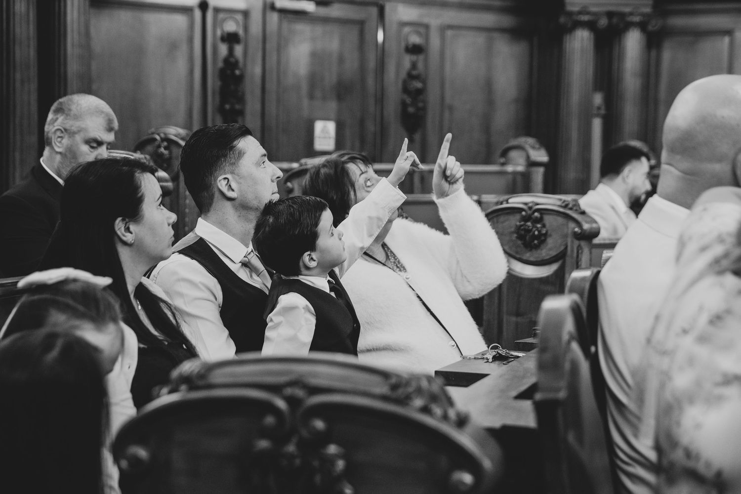 Black and white wedding photo of groom and groomsmen laughing joyfully inside an ornate church ceremony.