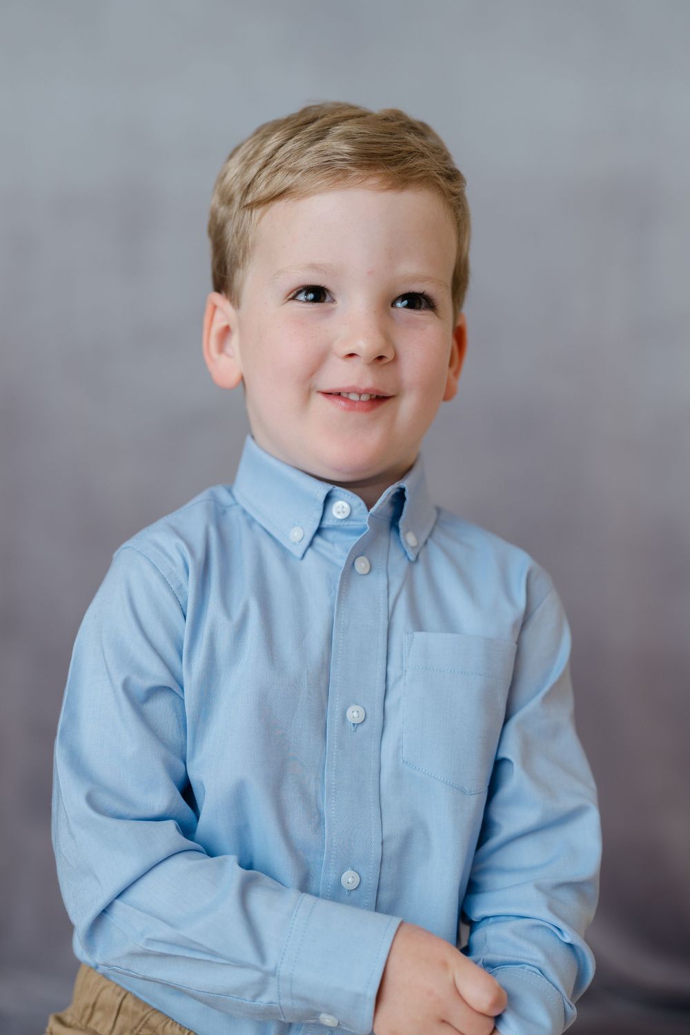 Cheerful young boy in light blue button-down shirt, studio portrait.