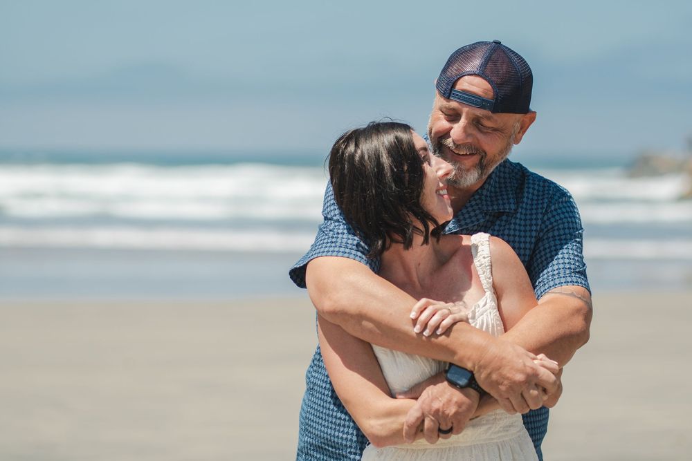 Happy couple embracing and dancing on a sunny beach, smiling and enjoying a romantic outdoor moment together. Oceanside, CA